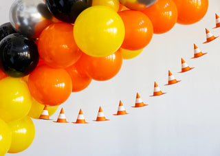 A bunch of yellow, orange, black, and silver balloons paired with a Construction Cone Banner by My Mind’s Eye hanging against a white background creates the perfect look for a construction-themed event.