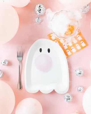 Paper plates shaped like ghosts alongside pink bubble gum, forks, a misty drink served with My Mind's Eye Cool Ghosts Cocktail Napkins, and disco balls are set on a pink backdrop with balloons. Perfect for a Halloween party filled with spooky fun!