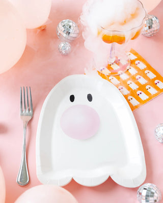 The Cool Ghosts Cocktail Napkin by My Mind’s Eye is laid out on a pink surface, with a fork on the left, surrounded by small disco balls, balloons, and a smoking glass of an orange drink—perfect for a spooky fun Halloween party!