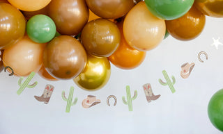 A ceiling decoration with large brown, green, and orange balloons, and a Cowboy Icon Banner from My Mind’s Eye featuring images of cacti, horseshoes, cowboy boots, and hats.