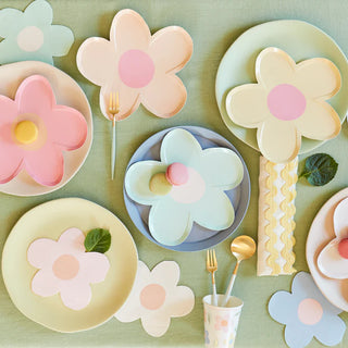 A spring-themed tablescape featuring floral-shaped plates in pastel hues, complemented by gold flatware and Meri Meri's Daisy Shaped Napkins, evokes a fresh, whimsical dining ambiance.