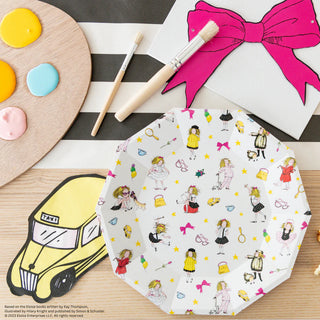 A decorated Eloise Large Plate from Daydream Society, featuring illustrated characters, sits on a table alongside art supplies, a yellow taxi cutout, and a canvas with a pink bow, reminiscent of scenes from the charming Eloise books set in the Plaza Hotel.