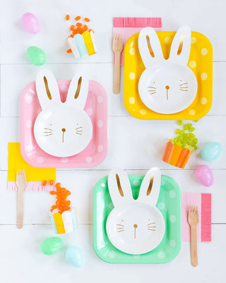 Colorful table setting with rabbit-themed plates and utensils, surrounded by candy and Easter eggs on a white wooden surface, accented with Fringe Napkins - Hip Hip Hooray napkins from My Mind's Eye.