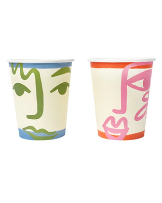 Two Pop! Party Supplies Art Face Party Cups with abstract designs. One has green lines on a light background; the other features pink lines with an orange band at the top. These unique and eye-catching cups are made from sustainable FSC paper, perfect for adding artistic flair to any gathering.