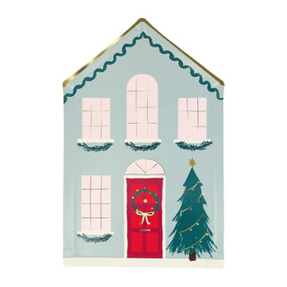 Illustration of a blue house with a red door, adorned with a Christmas wreath and large windows, perfectly represented on the Festive House Plates by Meri Meri. Outside stands a decorated tree, capturing the charm of wintry houses and evoking the warmth of festive meals shared on joyful occasions.