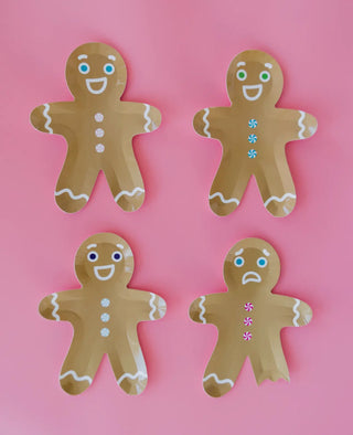 Four Gingerbread Man Plates from Jollity & Co rest on a pink background, each featuring unique colored buttons and facial expressions. Perfect for holiday desserts at Christmas parties, these plates bring a festive touch to any gathering.