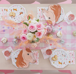 A table set for a party with horse-themed plates, Pony Tales Petite Napkins from the Daydream Society, a pink checkered tablecloth from the Pony Tales Collection, a bouquet of pink and white roses, and assorted snacks and decorations.