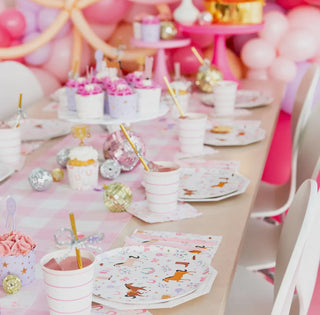 A decorated table set for a pastel pony party featuring Daydream Society's Pony Tales Small Plates, alongside pink-themed cups, cupcakes, and balloons.