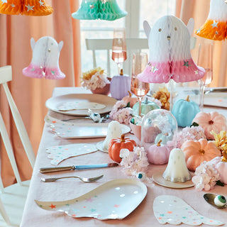 A festive table setup features ghost-shaped paper decorations, pastel pumpkins, floral arrangements, and star-themed tableware with silver foil details. Three ghost decorations hang above the table, complemented by Meri Meri's Ghost With Stars Napkins made from 3-ply paper.