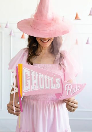 A person wearing a pink witch hat and dress holds the "Ghouls Rule Felt Pennant Banner" by My Mind’s Eye.