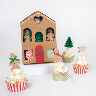 The Gingerbread Cupcake Kit by Meri Meri boasts festive toppers such as gingerbread men, trees, and stars. It includes four cupcakes adorned with white frosting and nestled in red and green liners, elegantly presented on a white surface.