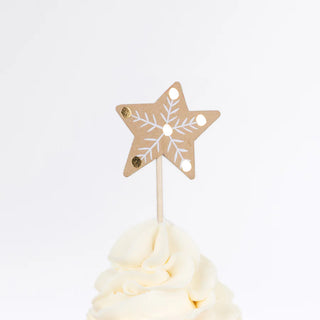 The festive topper features a paper star adorned with a snowflake design on a wooden stick, beautifully sitting atop a swirl of white frosting, making it the perfect addition to any Meri Meri Gingerbread Cupcake Kit.