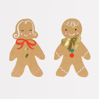 Two gingerbread cookies are decorated with icing bows and buttons. One has a red bow with pink details, and the other has a gold bow with red and green buttons. Add a festive touch to your Christmas party by pairing these cookies with Meri Meri's Gingerbread Napkins, embellished with gold foil details.