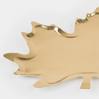 The Meri Meri Gold Maple Leaf Plates are decorative trays with a shiny, gold-colored surface and realistic details of a leaf's shape and edges. These elegant plates are perfect for adding sophistication to your fall party or Thanksgiving table decor. Set against a plain white background, they truly stand out.