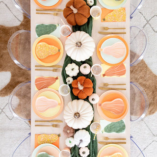 A dining table set for a meal with plates and utensils, decorated with pumpkins along the center and gourd-shaped place settings, featuring Jollity & Co's charming Gourd Large Napkins.