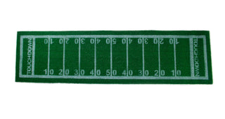 A green rectangular rug designed to resemble an American football field, with yard markings from 0 to 50 and the word "TOUCHDOWN" at both ends, perfect as a football party decoration or even a stylish Grass Football Table Runner by Talking Tables for your Super Bowl party.