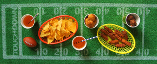 For a Super Bowl party, set up a football-themed table with nachos, skewered snacks, and drinks on a Grass Football Table Runner by Talking Tables for the perfect football party decoration.