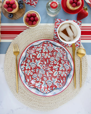 An overhead view of a table setting featuring vibrant My Mind's Eye Hamptons Floral Wave paper plates and gold cutlery, with bowls of berries and a drink nearby.
