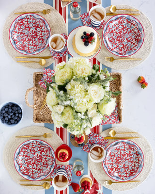 Overhead view of a beautifully set round dining table with floral plates, a bouquet of white roses in the center, and a cheesecake, arranged for four people, complemented by My Mind's Eye HAMPTONS FLORAL PAPER COCKTAIL NAPKINS.