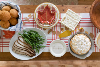 A table set for a Thanksgiving meal with bread rolls, green beans, sliced turkey, an elegant tablescape featuring plates with autumn leaf designs and gold foil edging, a lemon meringue pie, and a "thankful" Harvest Words Charger Plate by My Mind’s Eye.