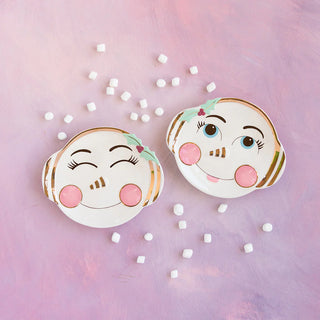 Two Glitterville Holly Jolly Cookie Plates with faces on them on a pink background.