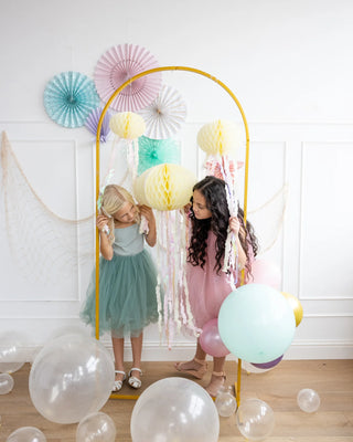 Two girls playing with decorative streamers in a festive room adorned with balloons and My Mind's Eye Honeycomb Jellyfish Set.