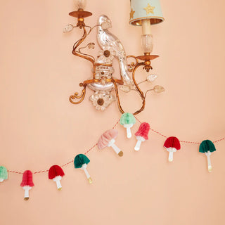 A wall adorned with a festive garland featuring a decorative light fixture and the Honeycomb Mushrooms Mini Garland by Meri Meri hanging below it.