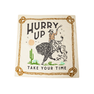 A Pop! Party Supplies Snake Catcher Bandana featuring a cowboy riding a buffalo with the text "Hurry Up" at the top and "Take Your Time" at the bottom. A desert scene with a cactus and sun completes this classic cowboy accessory.