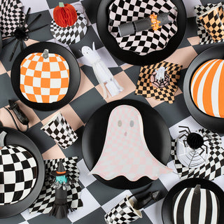 Create a table setting with a checkered black and white Halloween theme, featuring plates, cups, and retro decorations like ghosts, spiders, and pumpkins in various patterns. Add the perfect touch to your spooky party table with Meri Meri's Mod Pattern Pumpkin Napkins.