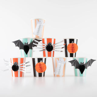 A set of nine Meri Meri Halloween Honeycomb Cups stacked in a pyramid formation. The cups are adorned with images of ghosts, spiders, bats, and pumpkins, featuring vibrant black, orange, and white colors with eye-catching 3D embellishments.