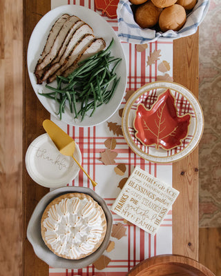 A Thanksgiving feast with a table setting featuring a plate of sliced turkey breast, green beans, a pie topped with whipped cream, rolls in a basket, Harvest Plaid 9" Round Plate by My Mind’s Eye, and a napkin that says "thankful.