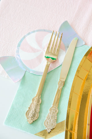 A decorative fork and knife rest on a napkin from the Jollity & Co Pink Peppermint Napkins collection, elegantly placed on a layered setting with pink, gold, and silver foil details.