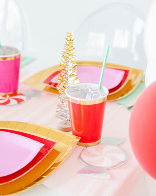 The table setting includes red and pink plates, a red cup with a straw, small silver Christmas trees, and Jollity & Co's Pink Peppermint Napkins featuring silver foil details on a light tablecloth.