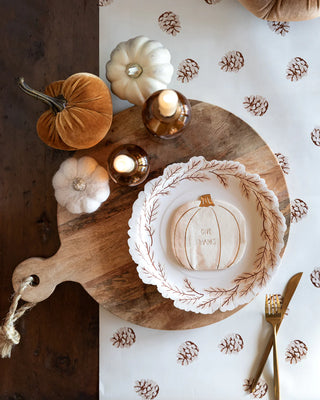 Create a festive Thanksgiving-themed table setting featuring Harvest Leaves Wreath Shaped Plates by My Mind’s Eye, complemented by candles and small pumpkins arranged on a wooden board with a patterned table cover.