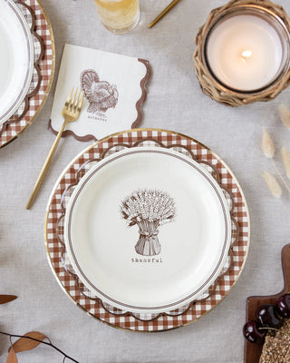 A Thanksgiving table set with "Thankful" plates, turkey napkin, gold fork, candle, and glass is enhanced by rustic Harvest Brown Gingham Check Plates from My Mind’s Eye and a touch of farmhouse style.