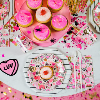 A festive table setup showcases cupcakes with pink frosting amid colorful decorations and neon hues. Enhance elegance with gold foil-pressed details, heart and floral napkins, Daydream Society's Love Notes Plates, and scattered confetti for a complete Valentine's Day scene.