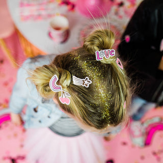 A child with two buns, decorated with Valentine's Day stickers and glitter from the Daydream Society love notes sticker set, shines against a pink background scattered with confetti and gold foil splashes that add extra sparkle.