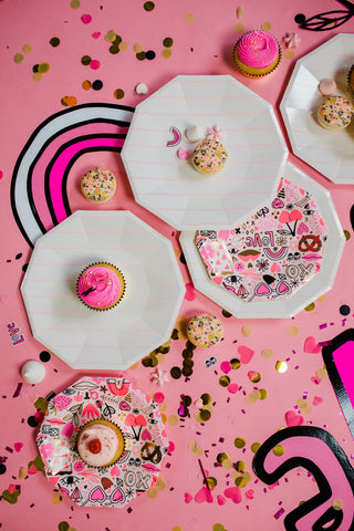 Love Notes Plates by Daydream Society, featuring decorated cupcakes and cookies, are set against a pink background adorned with gold foil-pressed elements, confetti, and graphic designs.