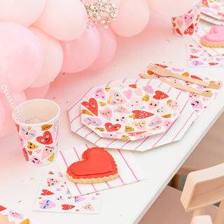 A festive table setting showcases Daydream Society's Heartbeat Gang Small Plates with neon and gold foil, heart-themed napkins and cups, plus a red heart-shaped cookie. Pink balloons enhance this Carolyn Suzuki-inspired scene.