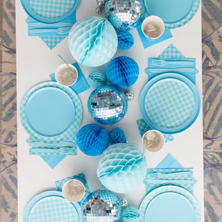 The table set for a flawless celebration includes Jollity & Co's "Check It! Out of the Blue Dessert Plates," featuring a blue and silver theme, checkered print napkins, matching plates, cups, utensils, and spherical ornaments.