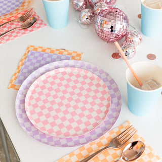 A table set with Check It! Purple Posse Dinner Plates by Jollity & Co, pastel napkins, blue cups, utensils, and disco ball decorations creates a lively ambiance for any gathering.