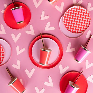 On a pink heart-adorned surface, Jollity & Co's Check It! Cherry Crush Dinner Plates and matching cups are elegantly paired with checkered print napkins from the Check It collection.