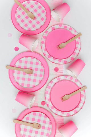 A festive arrangement of Neon Rose Pattern Plates - 7 inch party tableware from Oh Happy Day, including cups and wooden utensils, all set on a white background with a gingham pattern accent.