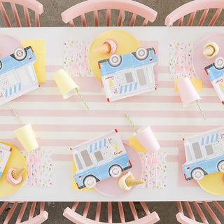 A party table set with pastel pink chairs, a striped tablecloth, holographic silver foil accents, Daydream Society's Ice Cream Dreams Large Plates, tipped over cups, straws, spoons, and scattered ice cream cones.