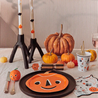 A vintage-look party table decorated for Halloween with a pumpkin centerpiece, pumpkin-themed paper plates, Halloween-themed napkins, Meri Meri's "It's Halloween!" cups with utensils, black candle holders, and small pumpkins.