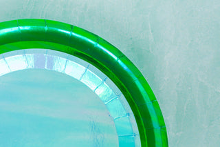 Close-up of a Jollity & Co's Posh Bubble Mint Round Plate, showcasing its green and iridescent surface with gold-foiled rims, set against a textured light green background.