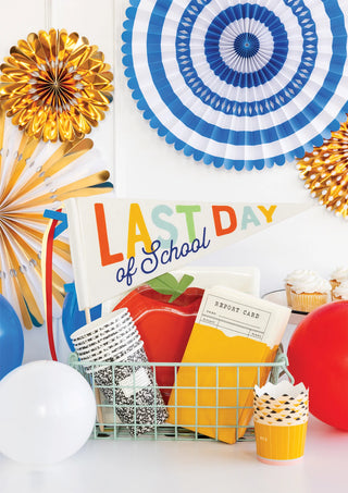 A festive display featuring a "My Mind's Eye Last Day of School Felt Pennant" banner, balloons, cupcakes, a report card, and decorative paper rosettes on a white background.