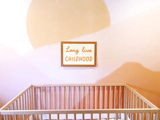 A wooden crib is positioned against a pastel-colored wall adorned with the Fun Club Long Live Childhood Banner.