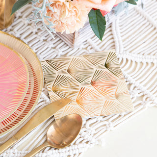 Elevate your table setting with Jollity & Co's La Boheme cocktail napkins, complemented by gold cutlery, pink and gold plates, and a geometric-pattern golden coaster on a white textured placemat. A floral arrangement adds charm to this exquisite party tableware ensemble.