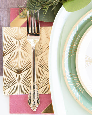 A silver fork rests on a Jollity & Co decorative napkin with fan patterns, next to La Boheme green and white plates with gold accents, perfect for elevating your summer birthday party tableware.